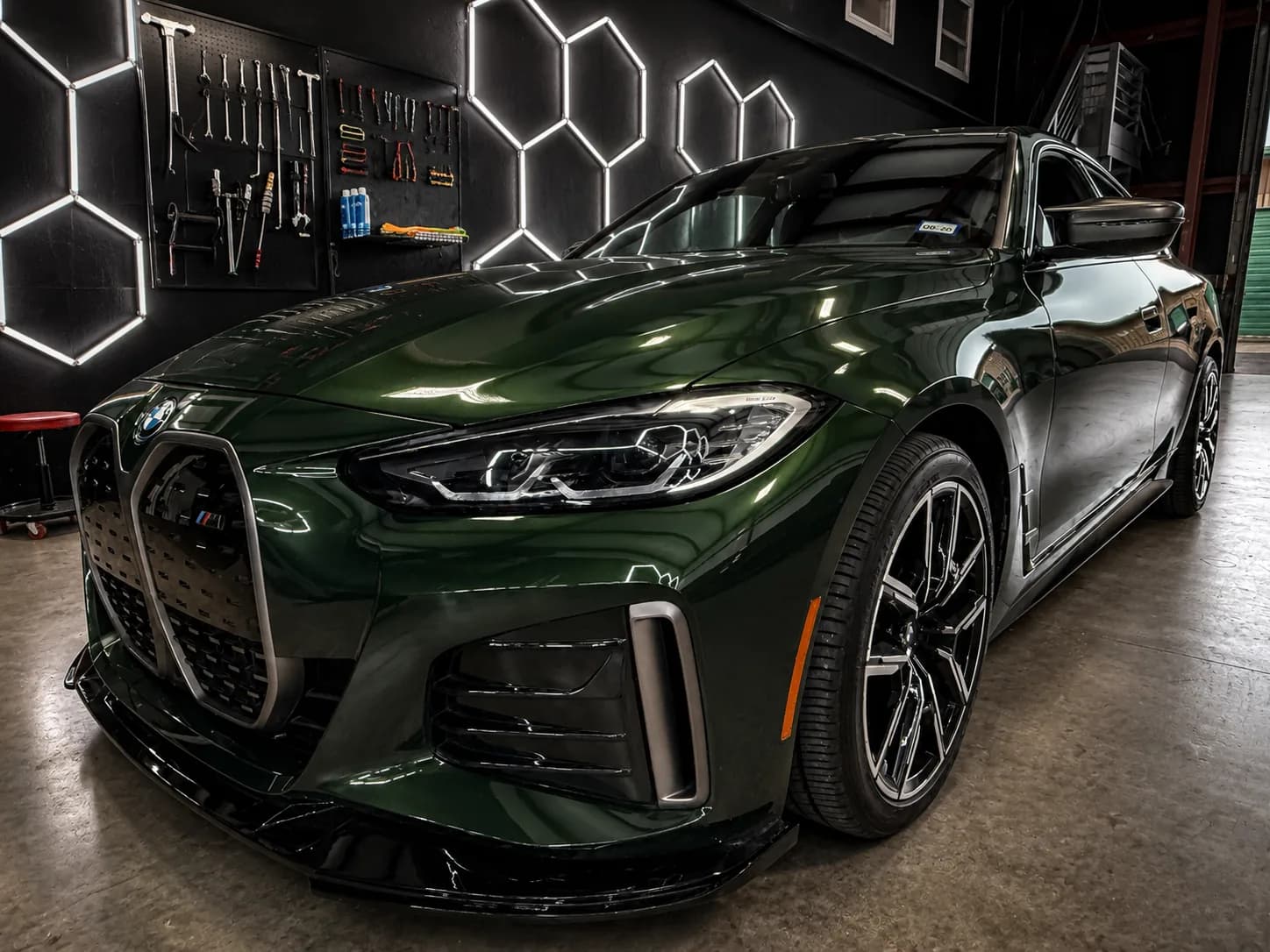 BMW under hexagonal lighting beside the tool wall in the Texas Dent Company Frisco repair shop