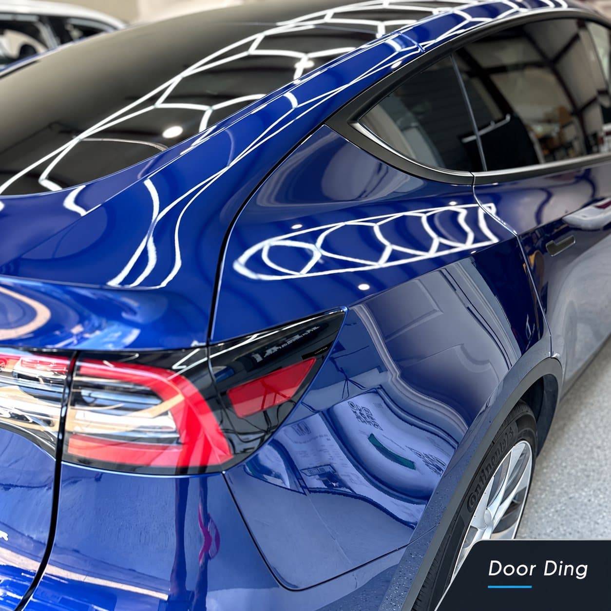 Blue Tesla rear quarter panel door ding under reflection lighting